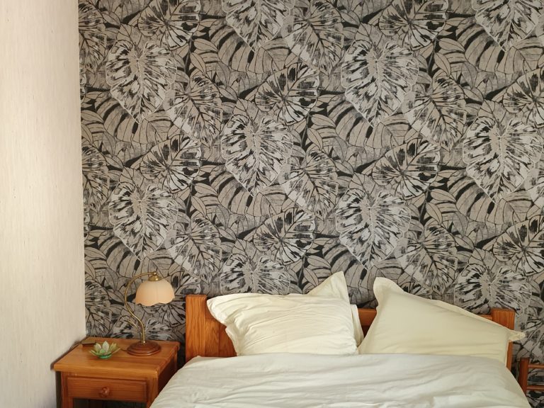 Photographie d'un mur d'une chambre avec un revêtement de grandes feuilles tropicales beiges